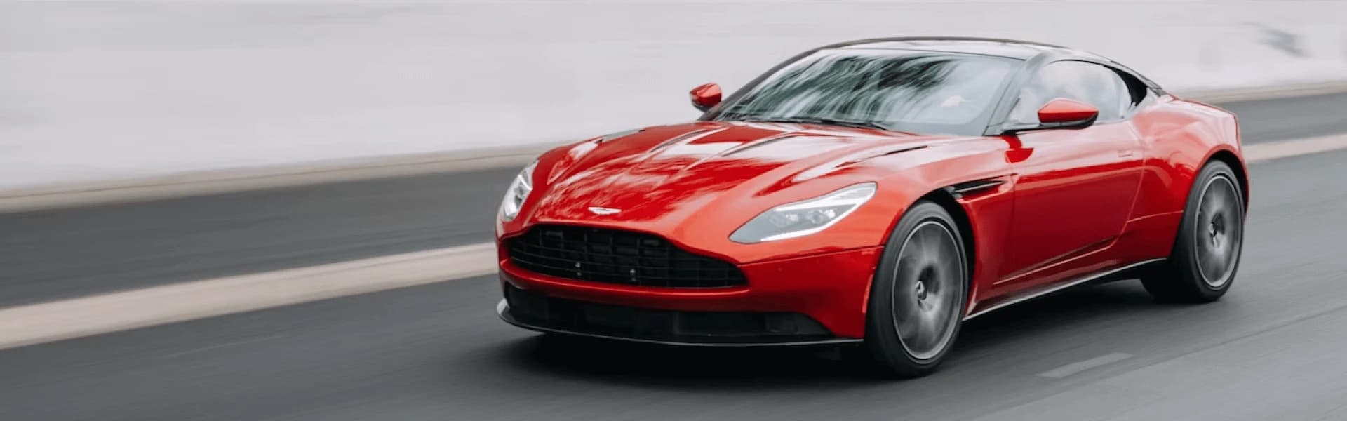 A red sports car is driving on a smooth road, with blurred background indicating motion.